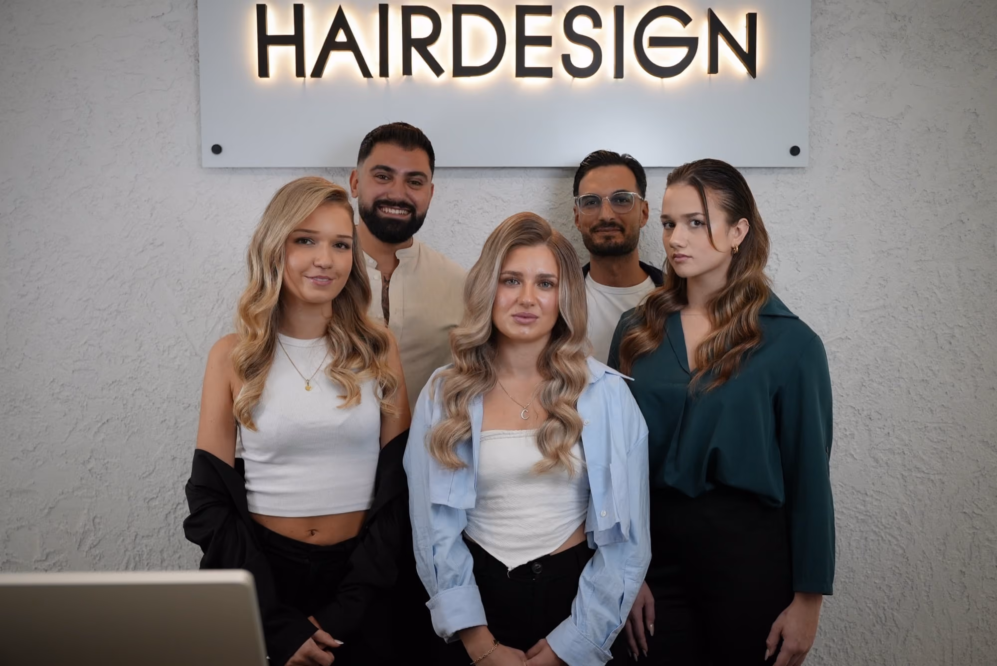 Teamfoto vor der Logo-Wand von Heiders Hairdesign